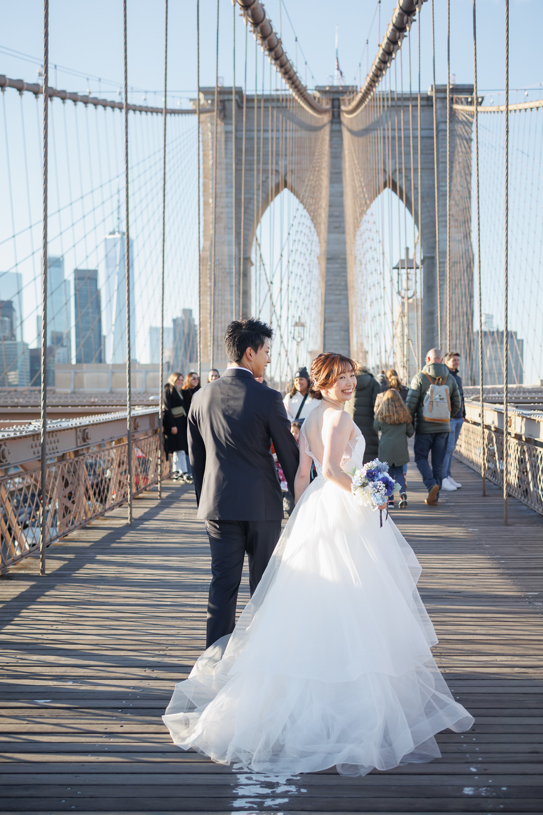 ニューヨーク前撮り/ウェディングフォト/鋼鉄ワイヤーの見事なデザインのブルックリンブリッジを歩くカップル。