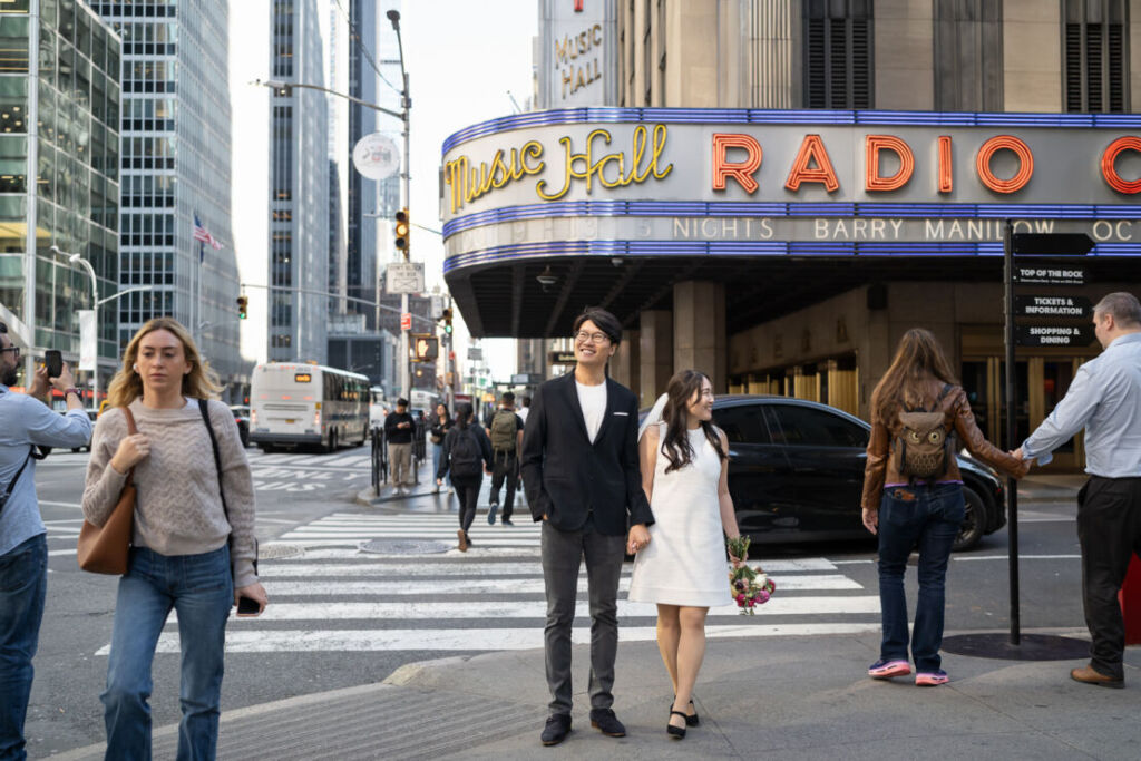 ニューヨークの前撮り/ウェディングフォト|RADIO CITY MUSIC HALL前で手をつなぐ花嫁と花婿。