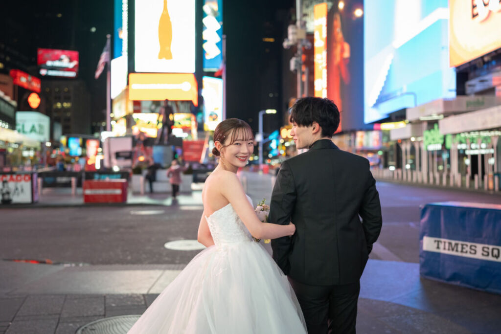 ニューヨークの前撮り|フォトウェディング/きらびやかなネオンの中腕を組む花嫁と花婿。
