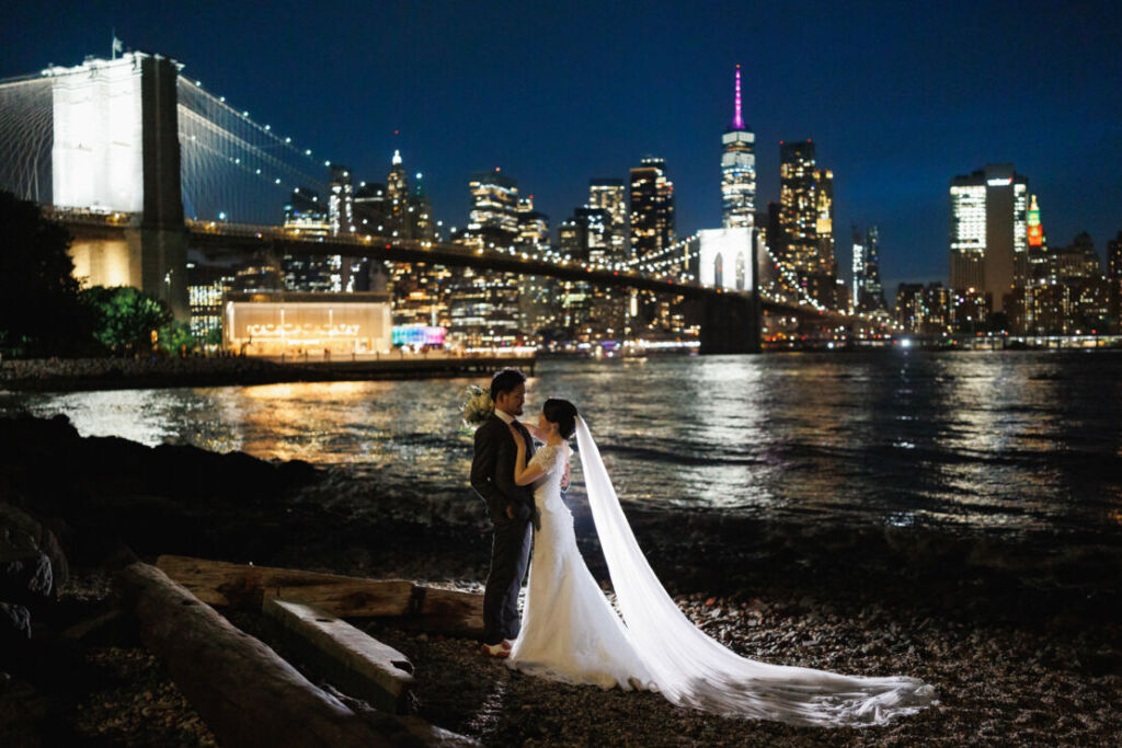 ニューヨークでウェディングフォト/ブルックリンブリッジパークからのマンハッタンの夜景を背景に立つカップル。