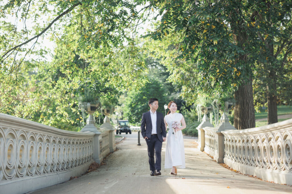 ニューヨークの前撮りウェディングフォト/ボウブリッジを手をつないで歩く花嫁と花婿。