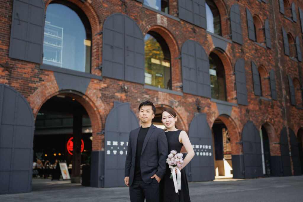 ニューヨークの前撮りウェディングフォト/DUMBOのレンガ造りの建物前に立つ花嫁と花婿。