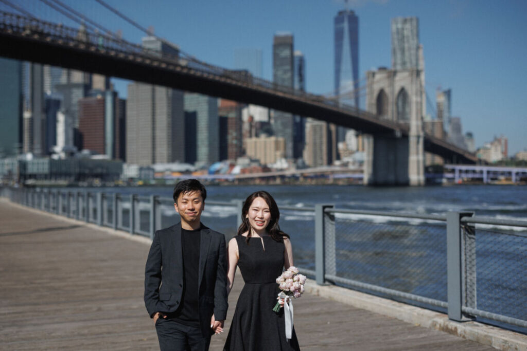 ニューヨークの前撮りウェディングフォト/ブルックリンブリッジパークを手をつないであるくカップル。