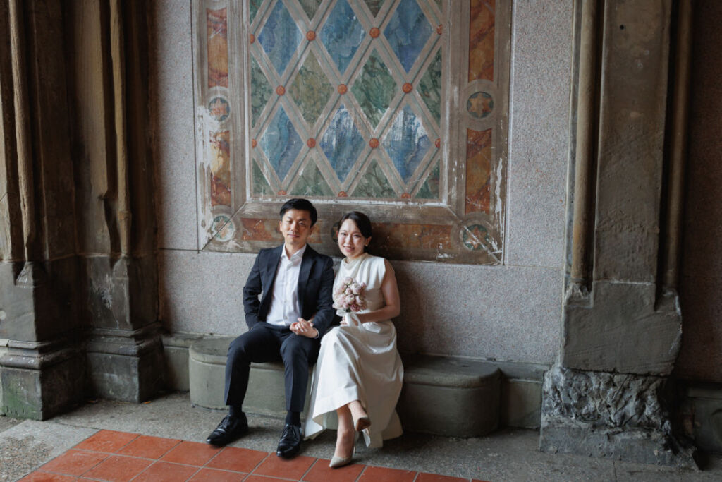 ニューヨークの前撮りウェディングフォト/ベセスダテラスの壁画前に座るカップル。