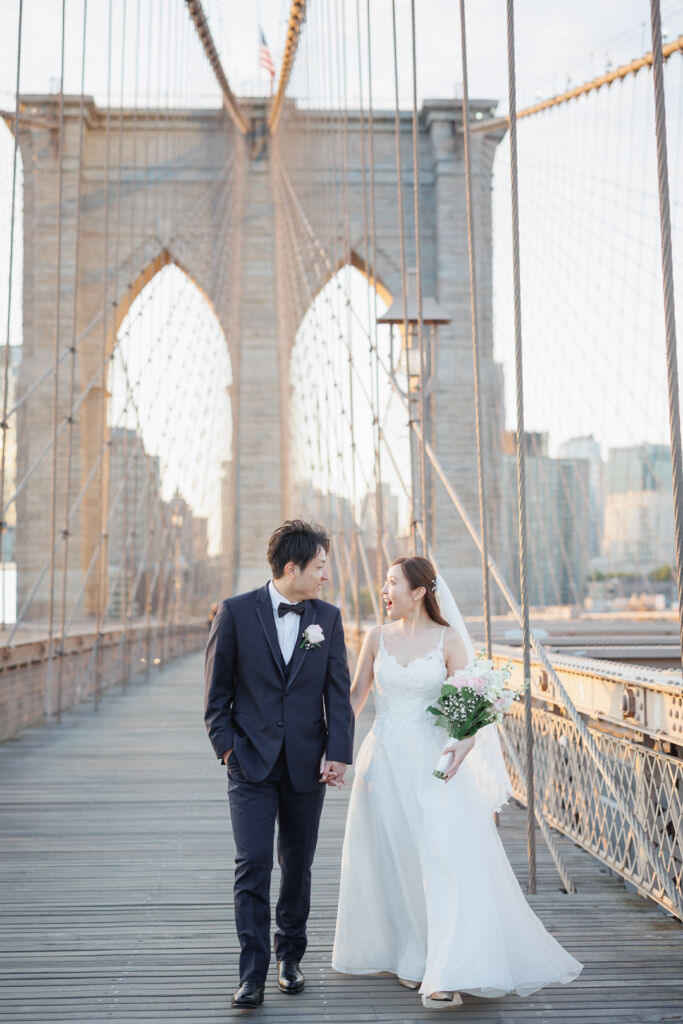 ニューヨークのウェディングフォト|前撮り/ブルックリンブリッジで手をつないで歩く花嫁と花婿。
