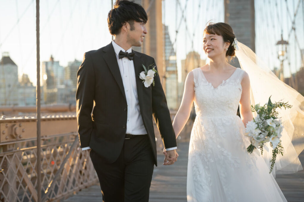 ニューヨークの前撮り|ウェディングフォト/ブルックリン橋を手をつないで歩く花嫁と花婿。