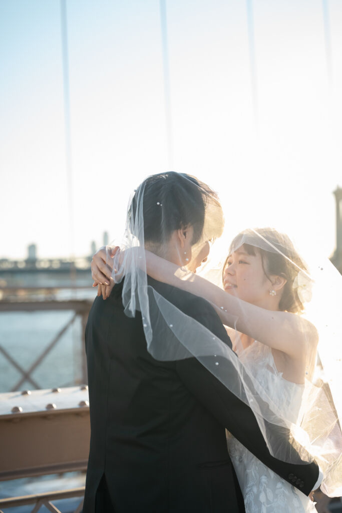ニューヨークの前撮り|ウェディングフォト/ブルックリン橋でベールをかぶる花嫁と花婿。