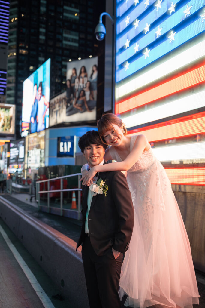 ニューヨークの前撮り|ウェディングフォト/タイムズスクエアのネオンサインの前で笑顔が輝く花嫁と花婿。