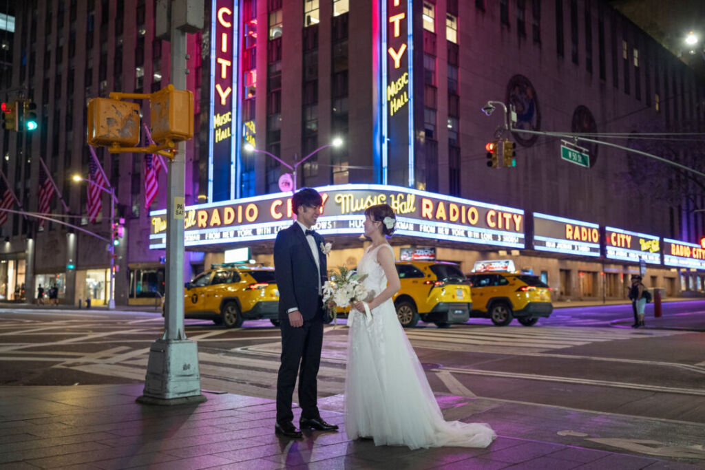 ニューヨークの前撮り|ウェディングフォト/ラジオシティホール前に立つ花嫁と花婿。