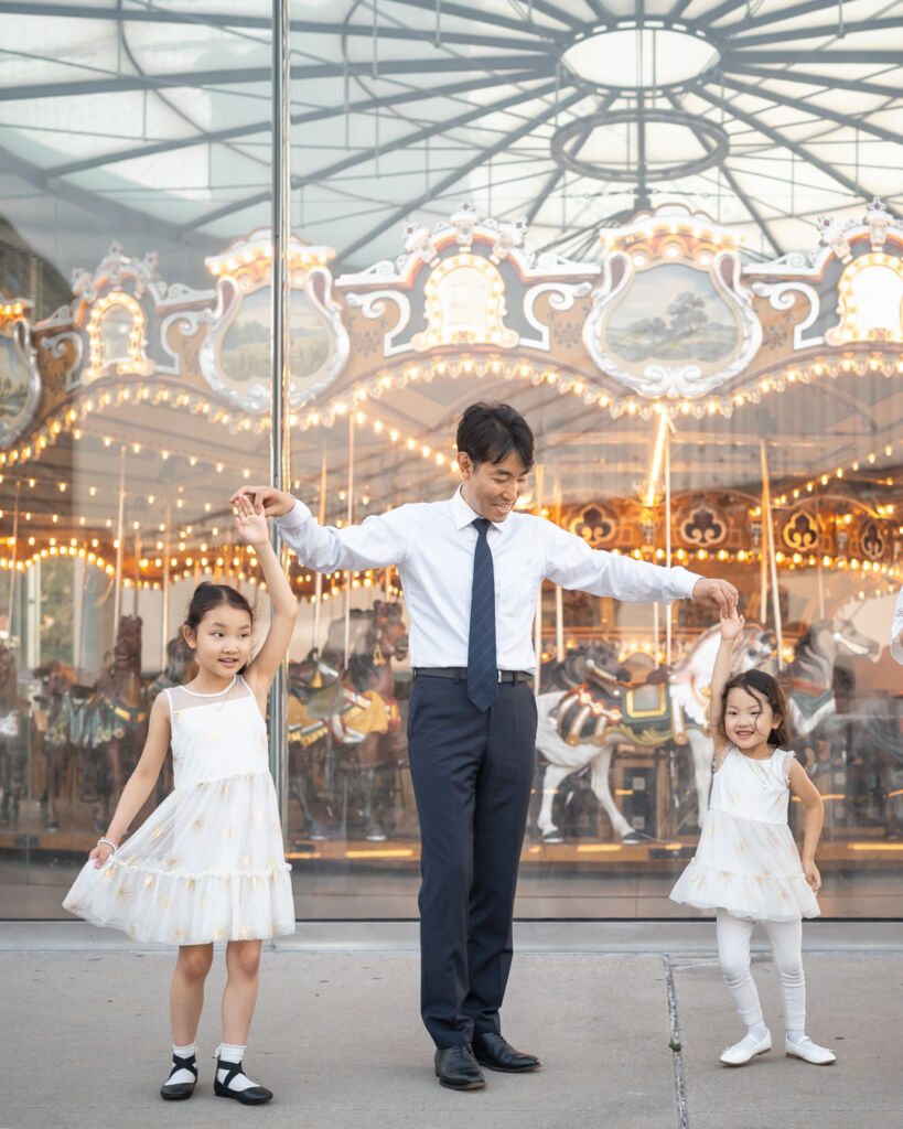 ニューヨークのファミリーフォト/ジェーンズカルーセルの前でポースをとるお姉ちゃんと妹ちゃん。