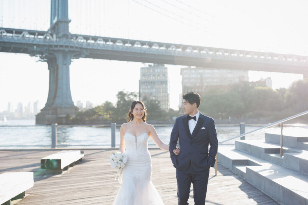 ニューヨークのフォトウェディング|前撮り/ブルックリンブリッジパークを腕を組んで歩く花嫁と花婿。