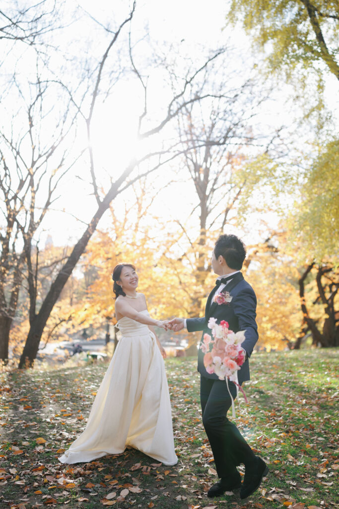 ニューヨークの前撮り|ウェディングフォト/ボウブリッジのそばの芝生エリアで手をつなぐ花嫁と花婿。