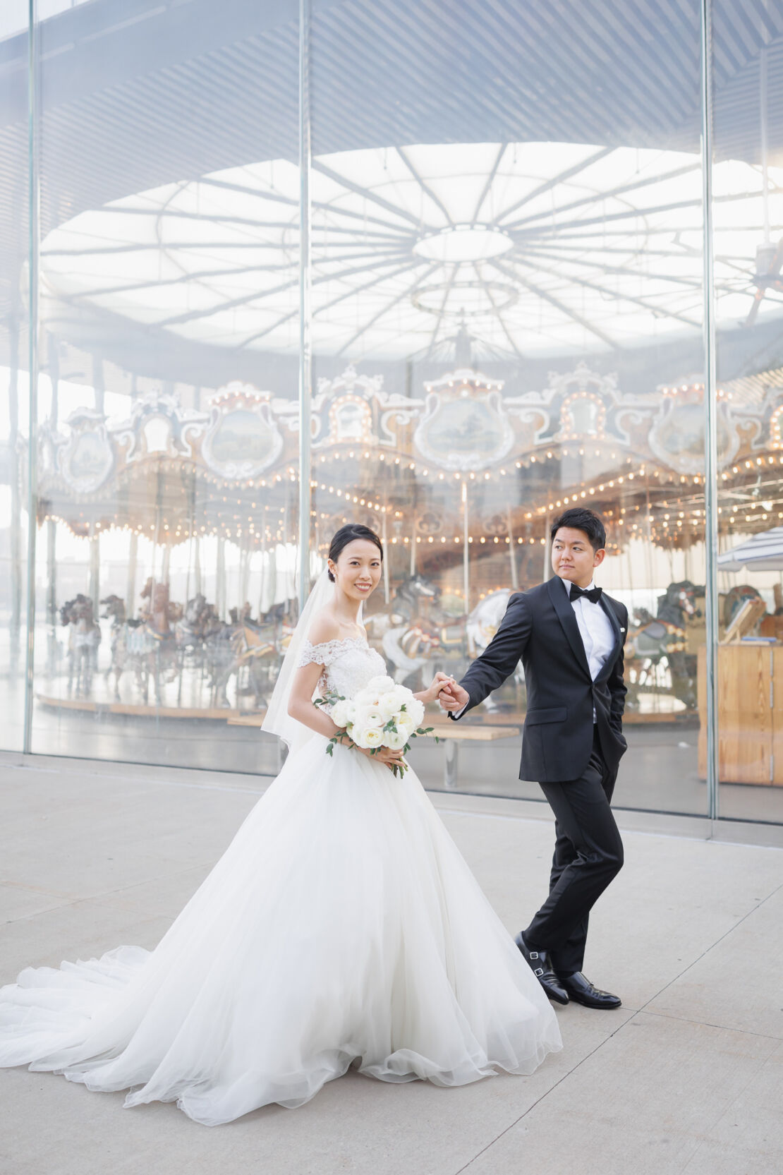 NYウェディングフォト|前撮り/メリーゴーランドの前を歩く花嫁と花婿。