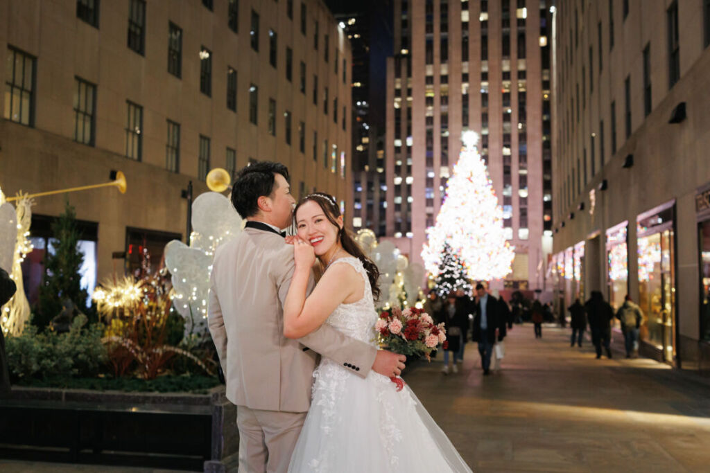 ニューヨークの前撮り|ウェディングフォト/クリスマスツリーを背景に寄り添う花嫁と花婿。